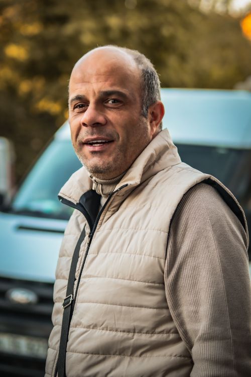 Free Smiling man in a beige vest standing outdoors with a car in the background on a fall day. Stock Photo