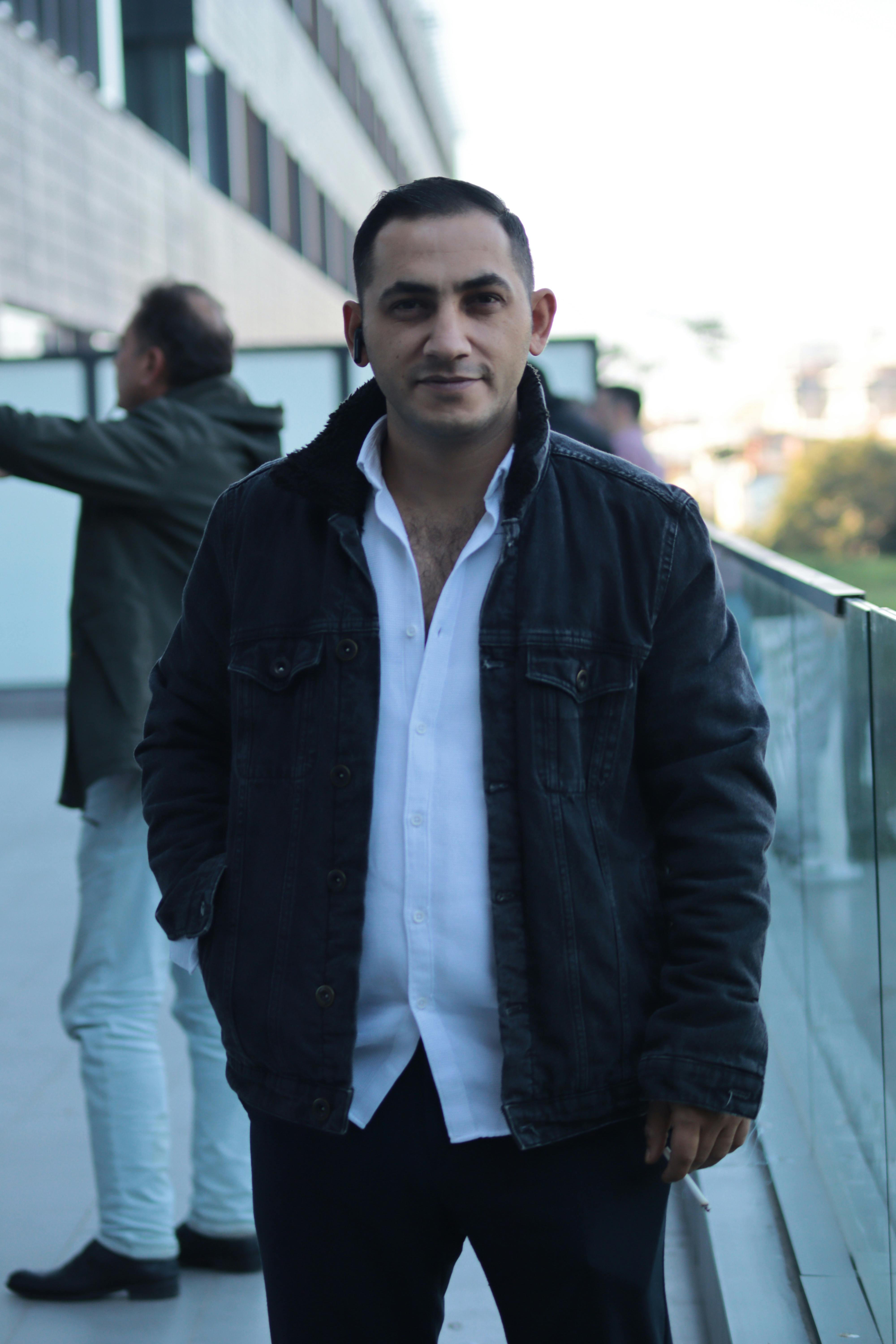 A man in a casual denim jacket standing outdoors on a modern building balcony.