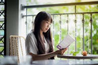 这幅肖像画描绘了一位妇女在阳光明媚的阳台上读书，周围绿植环绕，画面宁静