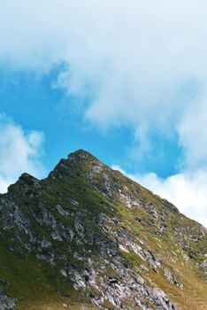 Stunning view of a grassy mountain peak under a bright blue sky with clouds.