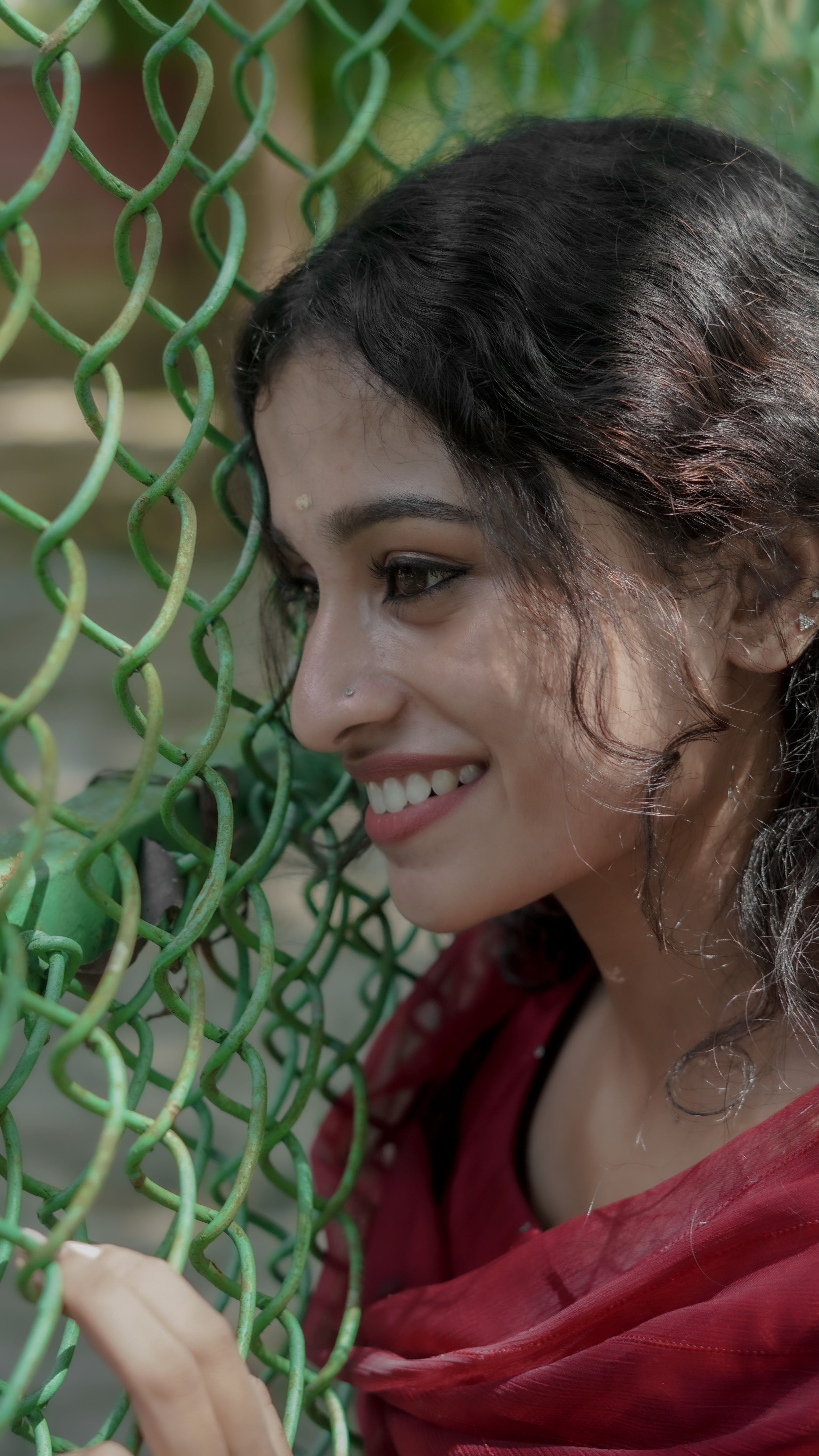 A woman in a red outfit smiles beside a green chain-link fence outdoors.