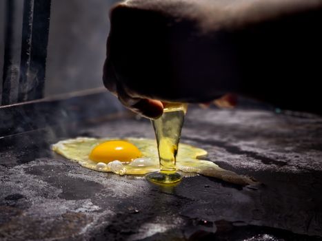 A hand cracks a raw egg onto a sizzling hot griddle, perfect for food-related imagery.