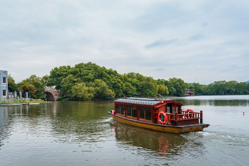 Free Scenic view of a traditional wooden boat on West Lake, Hangzhou, highlighting lush greenery and calm water. Stock Photo