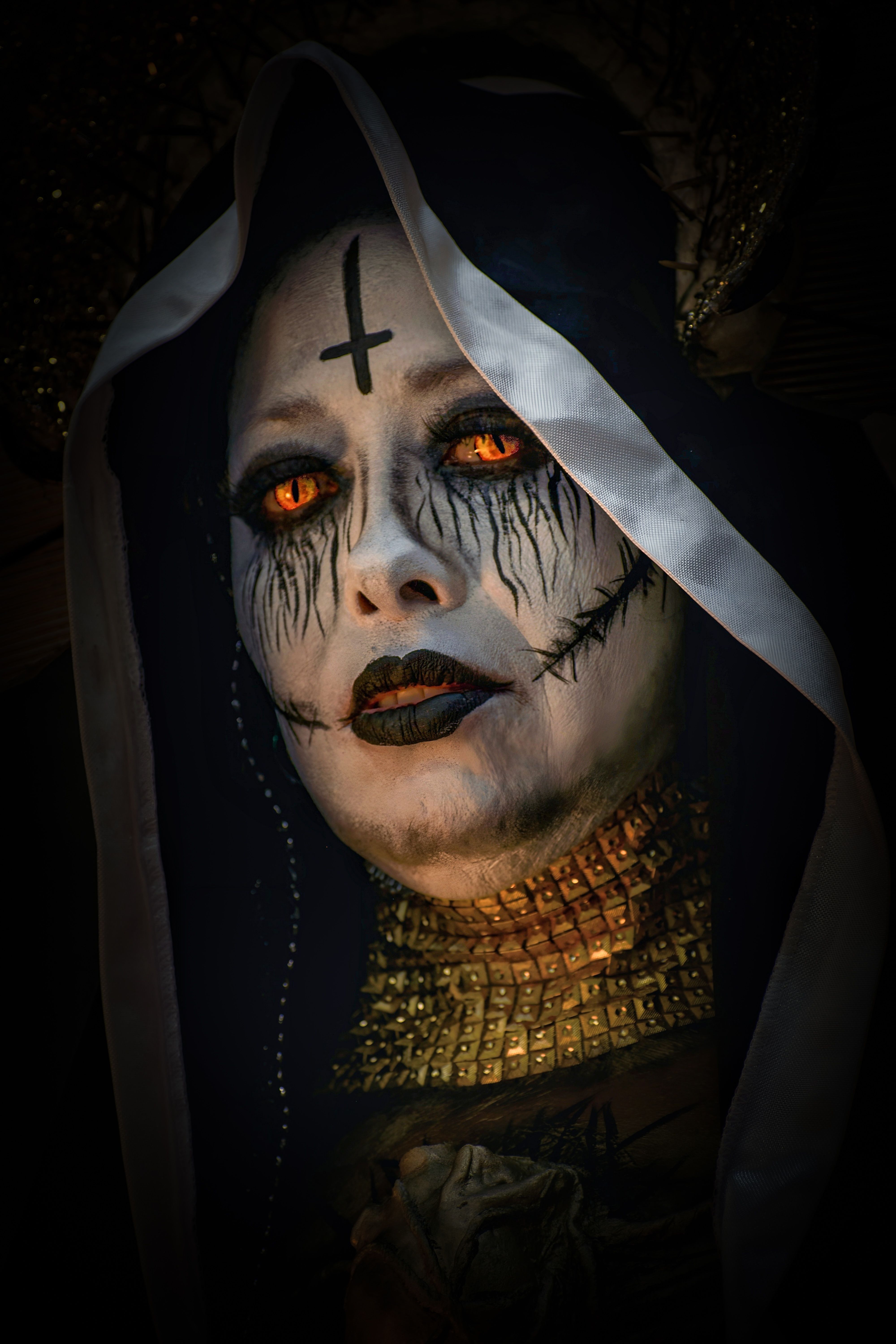 Close-up of a sinister Halloween character with intense makeup and golden accessories, captured in dramatic lighting.