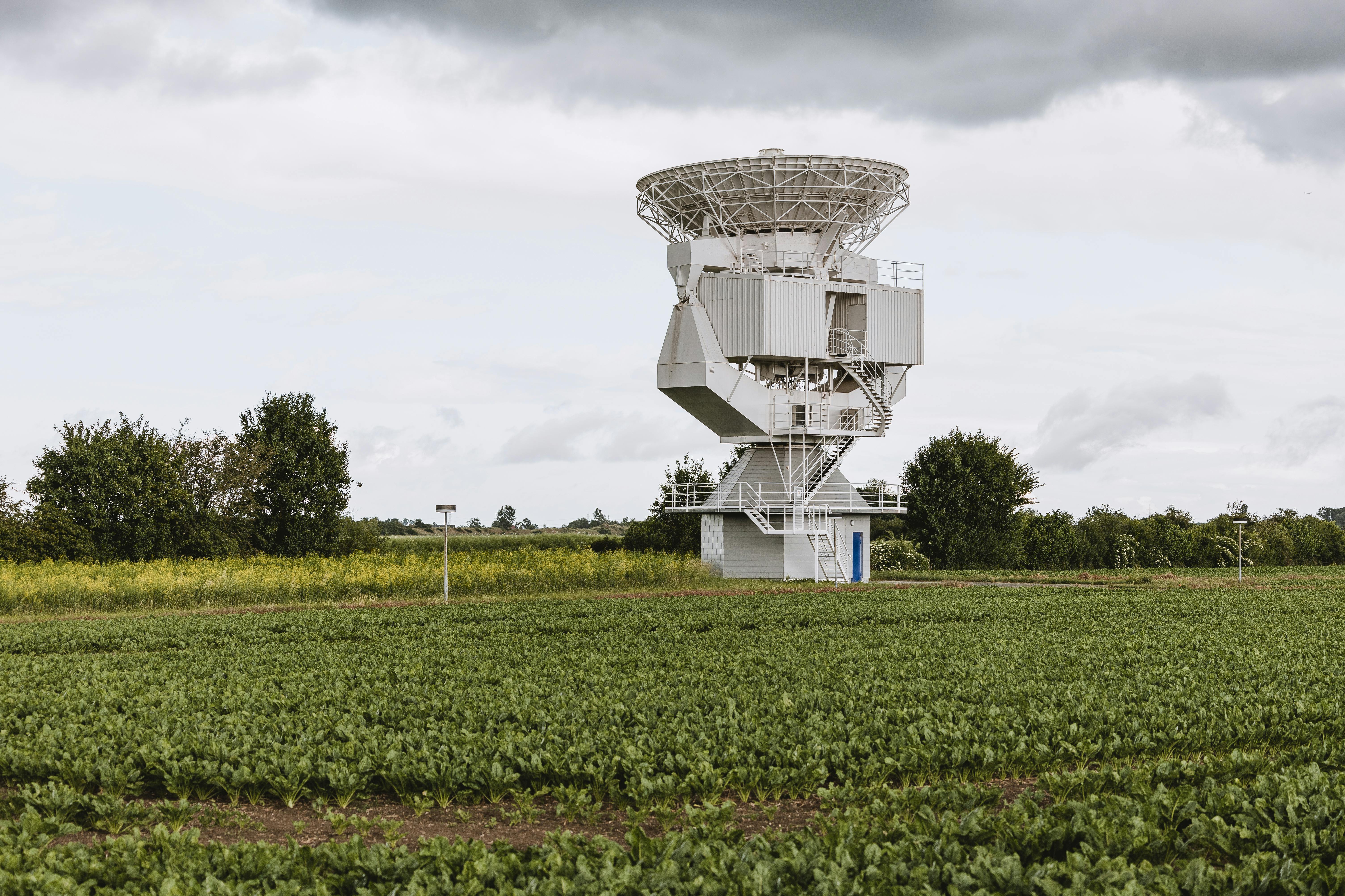 A large satellite antenna stands prominently in a lush field in Riedstadt, Germany.