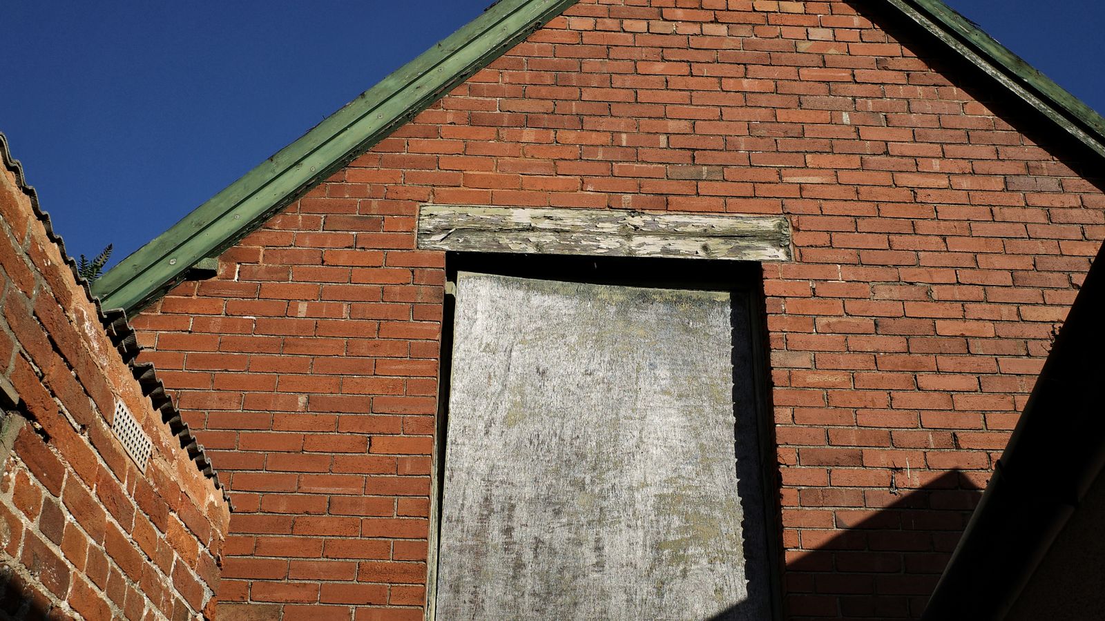 Façade d'un bâtiment en brique ancienne dont une fenêtre a été condamnée par des planches.