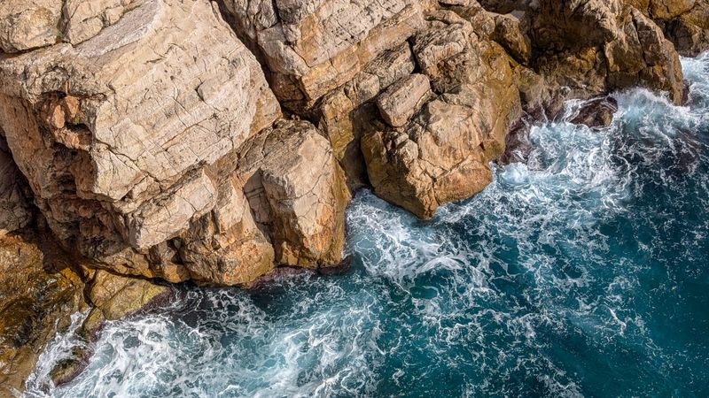 Waves crashing against a rugged sea cliff — photo by Robert Carnes on Pexels