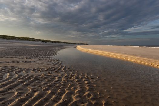 Tranquil beach scene in Kampen, Sylt, featuring dramatic clouds and rippled sand.