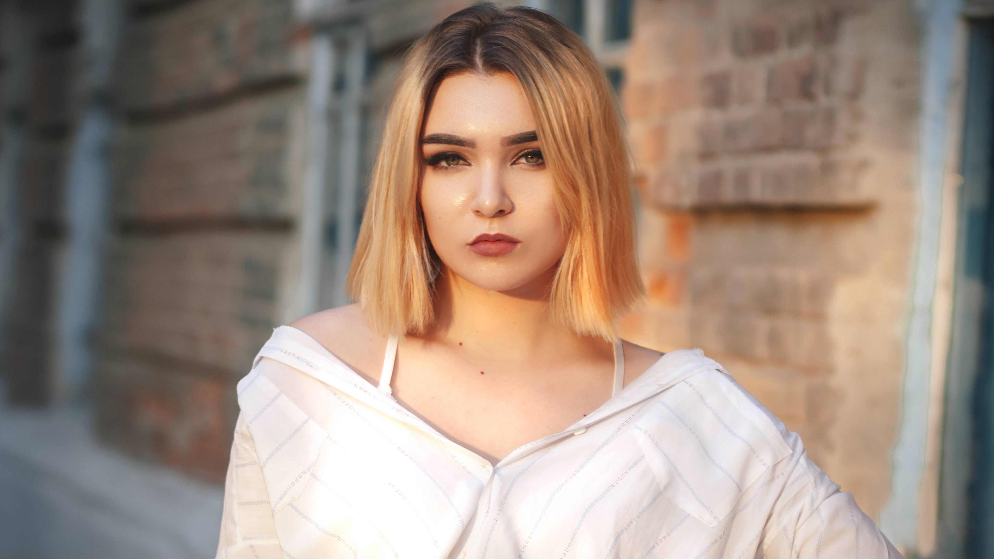 Close-up portrait of a woman wearing a white shirt standing outdoors against a brick wall.