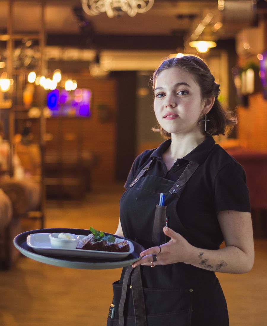 Server carrying a tray of plates through a warmly lit restaurant