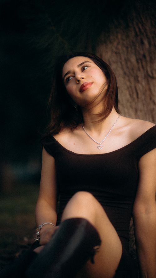 Free A serene portrait of a woman in a black dress leaning against a tree, captured during the day. Stock Photo