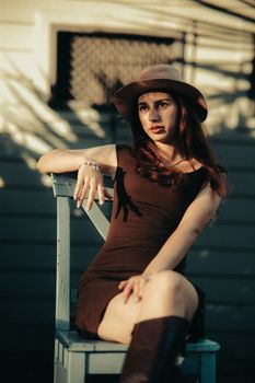 Portrait of a stylish young woman sitting on a chair outdoors, in warm sunlight.