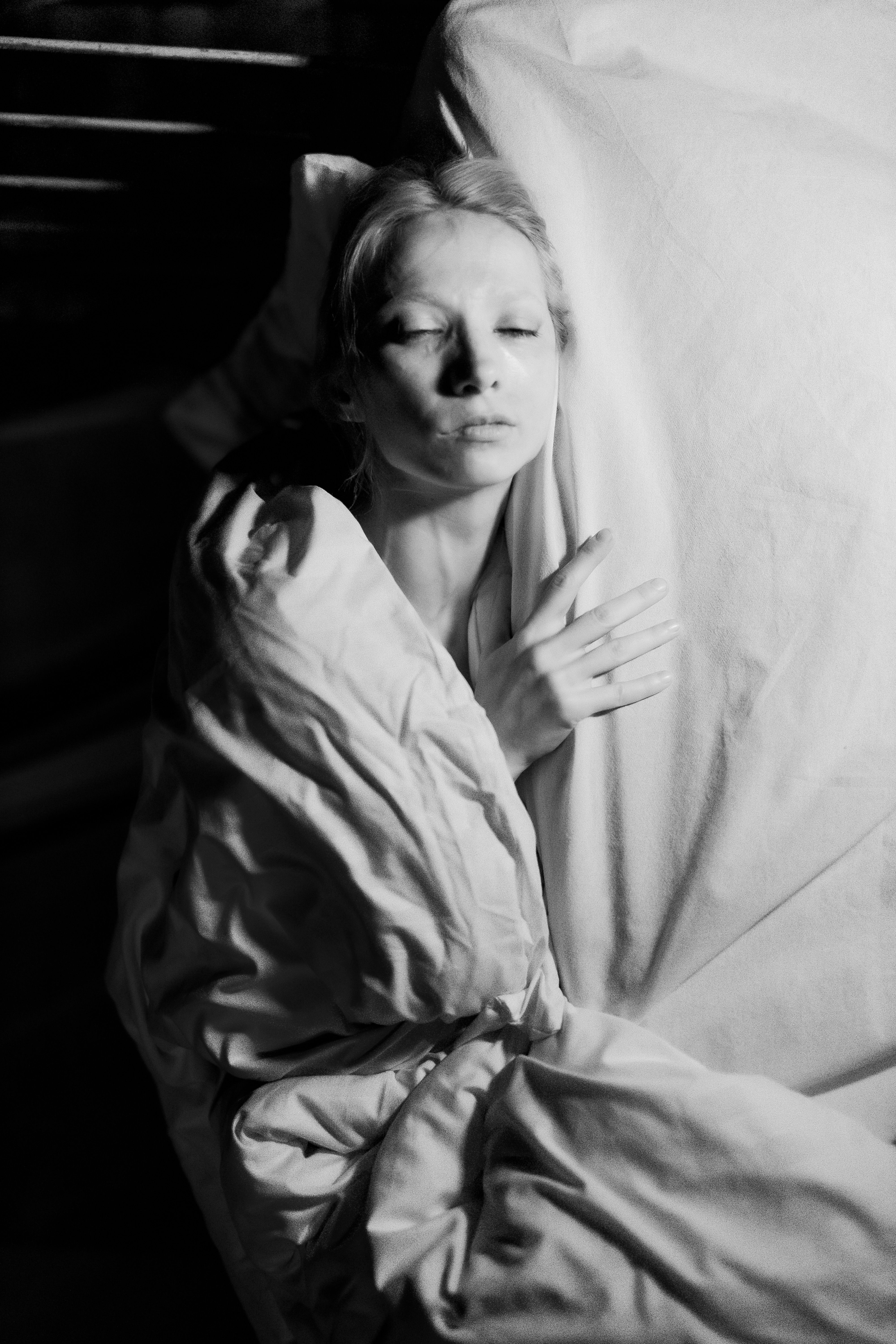 Moody black and white portrait of a woman wrapped in a blanket, creating a dramatic and intimate atmosphere.