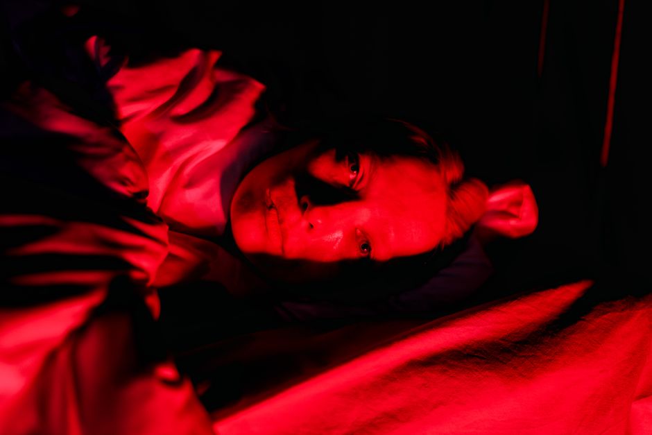 Whoop 5.0 vs Oura Ring 4: Sleep Tracking Accuracy Showdown (2024) A person in bed is illuminated by bold, red lighting creating a vivid, dramatic portrait.
