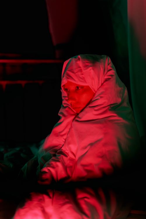 Free A cozy scene featuring a person wrapped in a blanket with dramatic red lighting, creating a moody atmosphere. Stock Photo