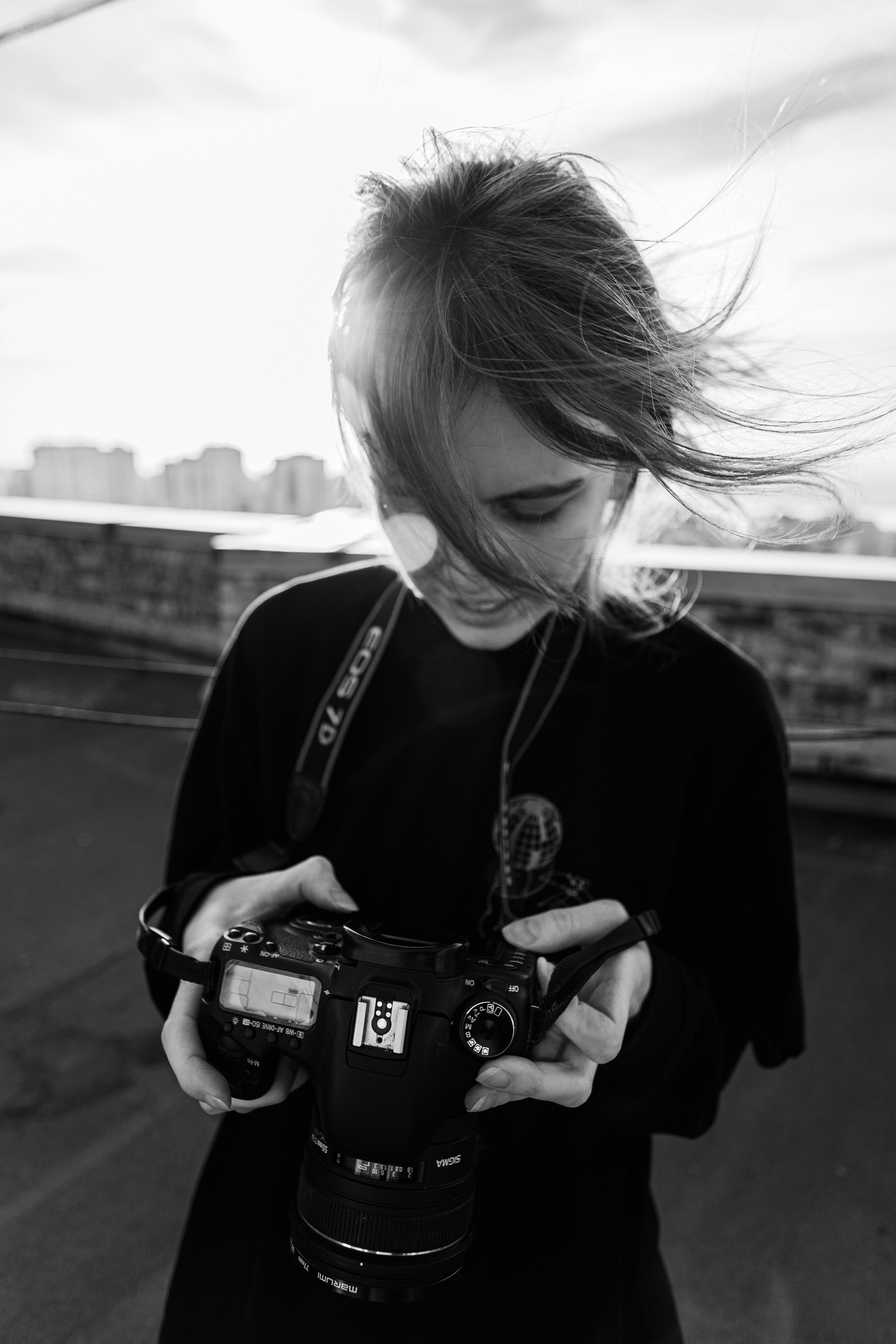 Black and white image of a young photographer on a rooftop holding a DSLR camera.