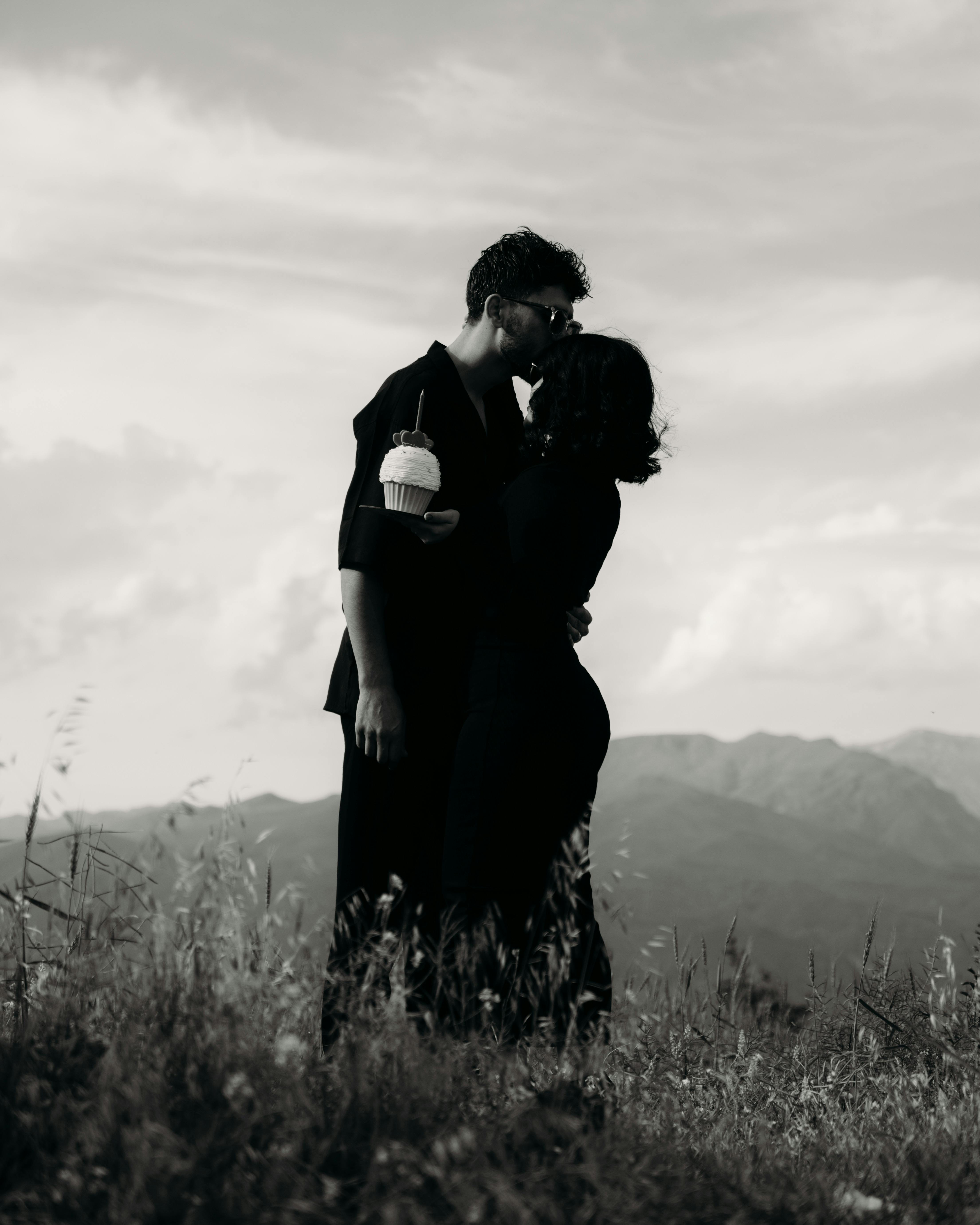 A romantic black and white photograph of a couple sharing an intimate moment on a grassy hilltop.