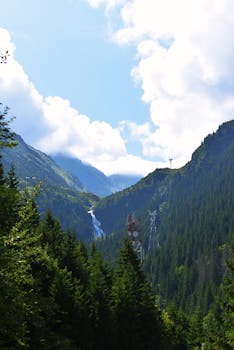 明亮的天空下，郁郁葱葱的青山、瀑布和输电塔构成了一幅令人惊叹的景观