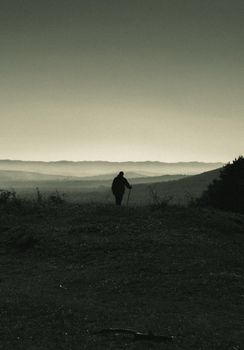 Lonely hiker silhouetted against mountain landscape with walking stick.