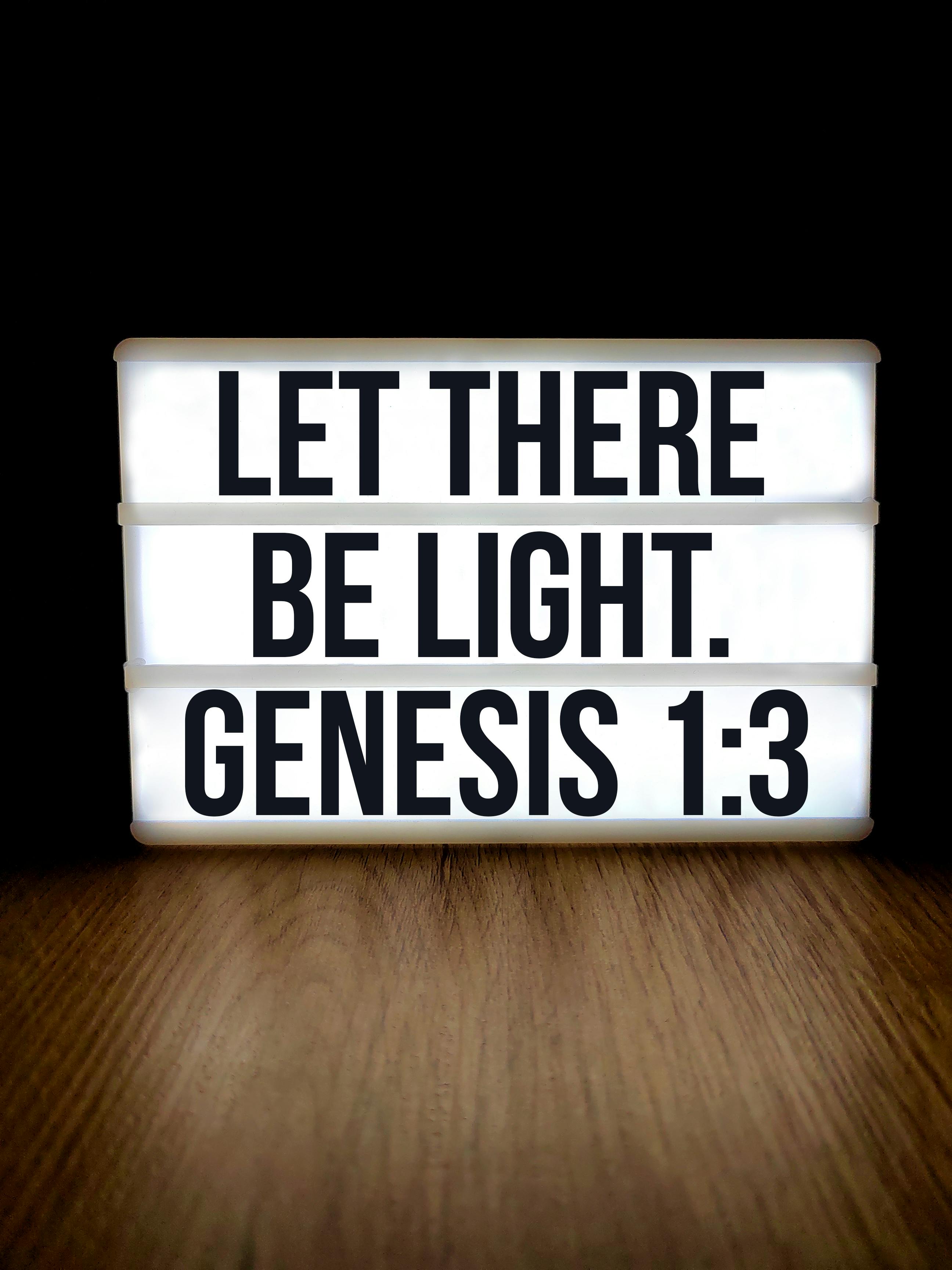 Free Lightbox displaying Genesis 1:3 'Let There Be Light' on a wooden surface. Stock Photo
