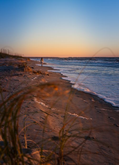 Free Person walks alone on a tranquil beach at sunset with waves gently lapping the shore. Stock Photo