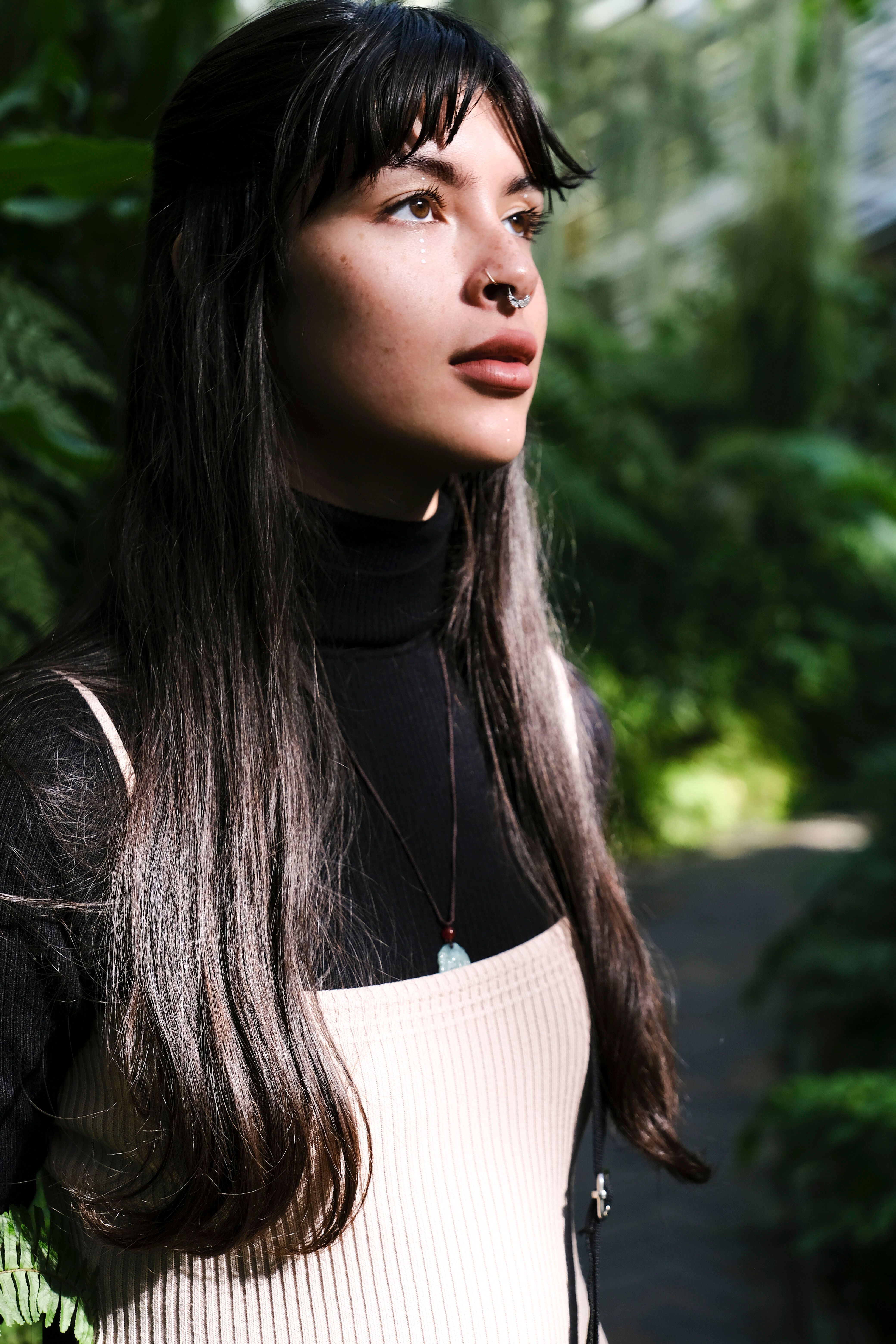 A thoughtful woman in a cozy sweater surrounded by lush greenery, basking in natural light.