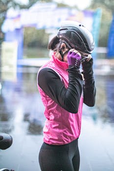 Female cyclist preparing for ride, adjusting helmet outdoors in rainy weather.