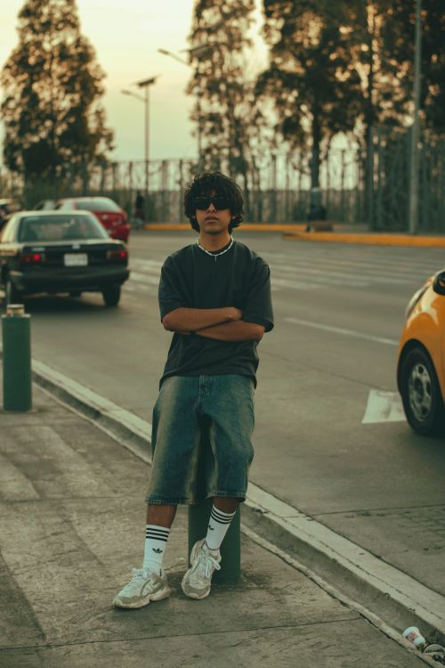 Free Teen boy in casual streetwear stands confidently on city street at sunset. Stock Photo