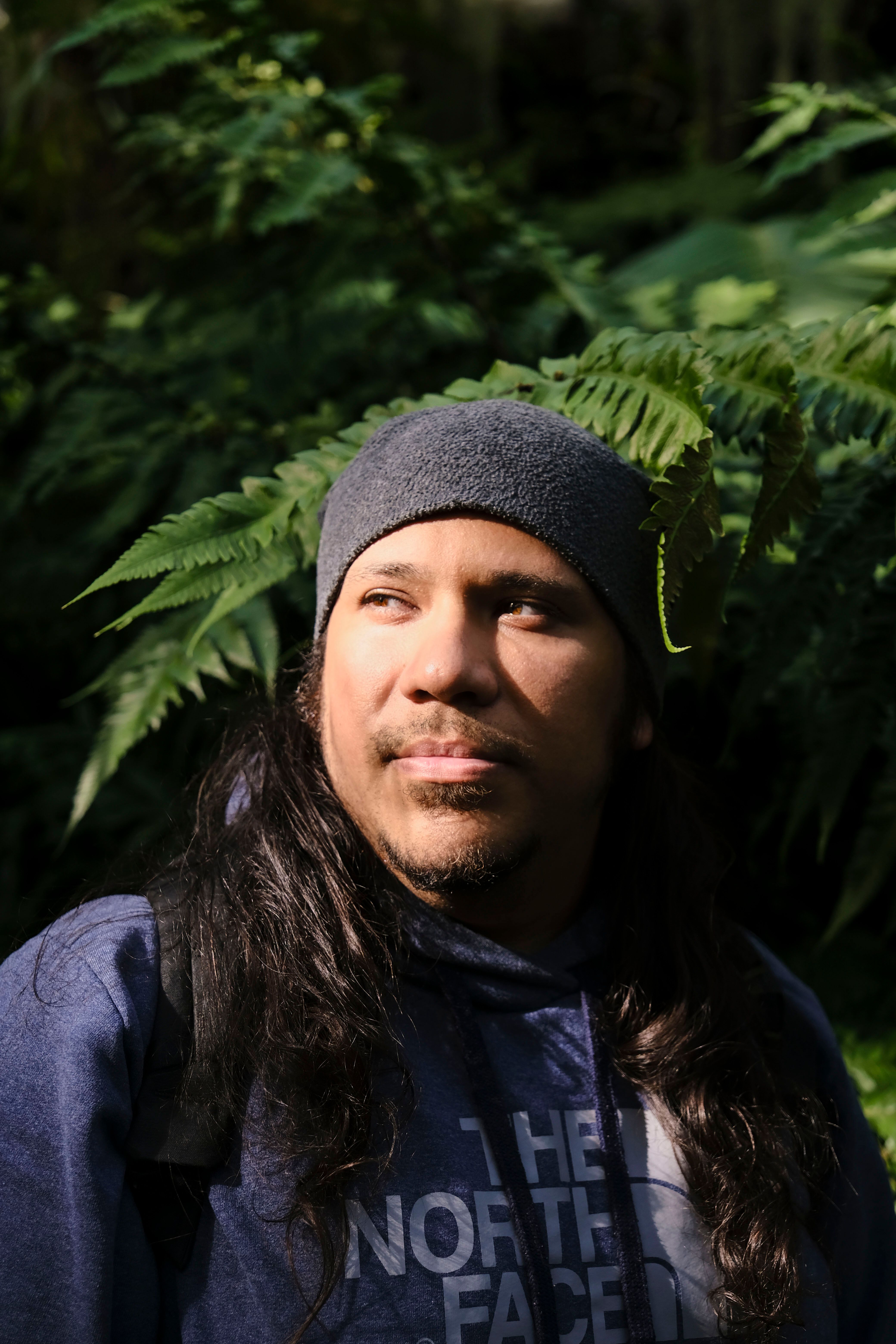 Close-up portrait of a man surrounded by vibrant ferns, basking in natural light.