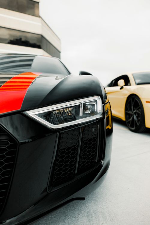 Free A detailed shot of a black luxury sports car with red accents, parked beside a yellow car. Stock Photo