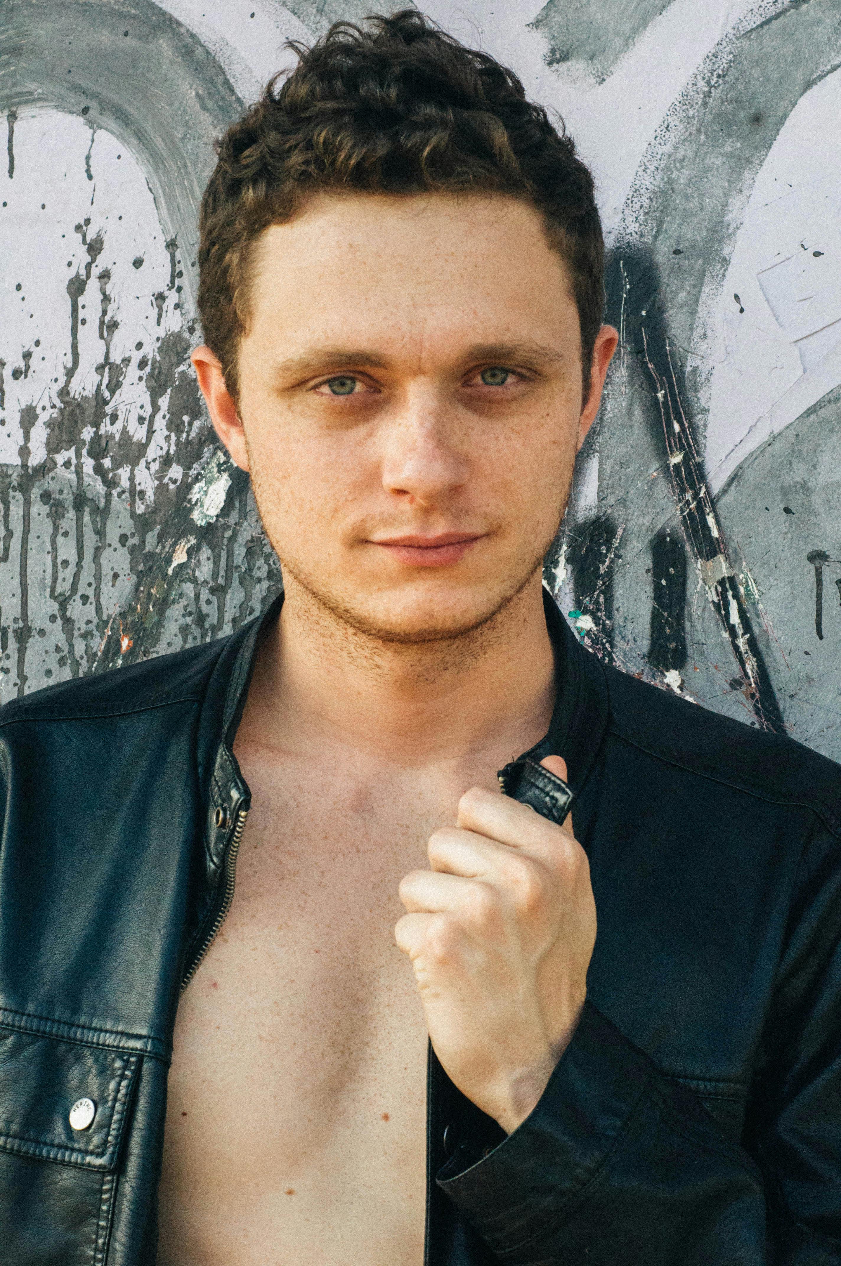 Portrait of a young man in a leather jacket standing in front of a graffiti wall, looking confident.
