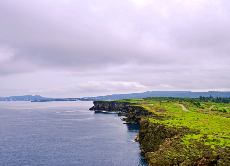 Explore the breathtaking coastal cliffs of Okinawa, showcasing lush greenery and the ocean.