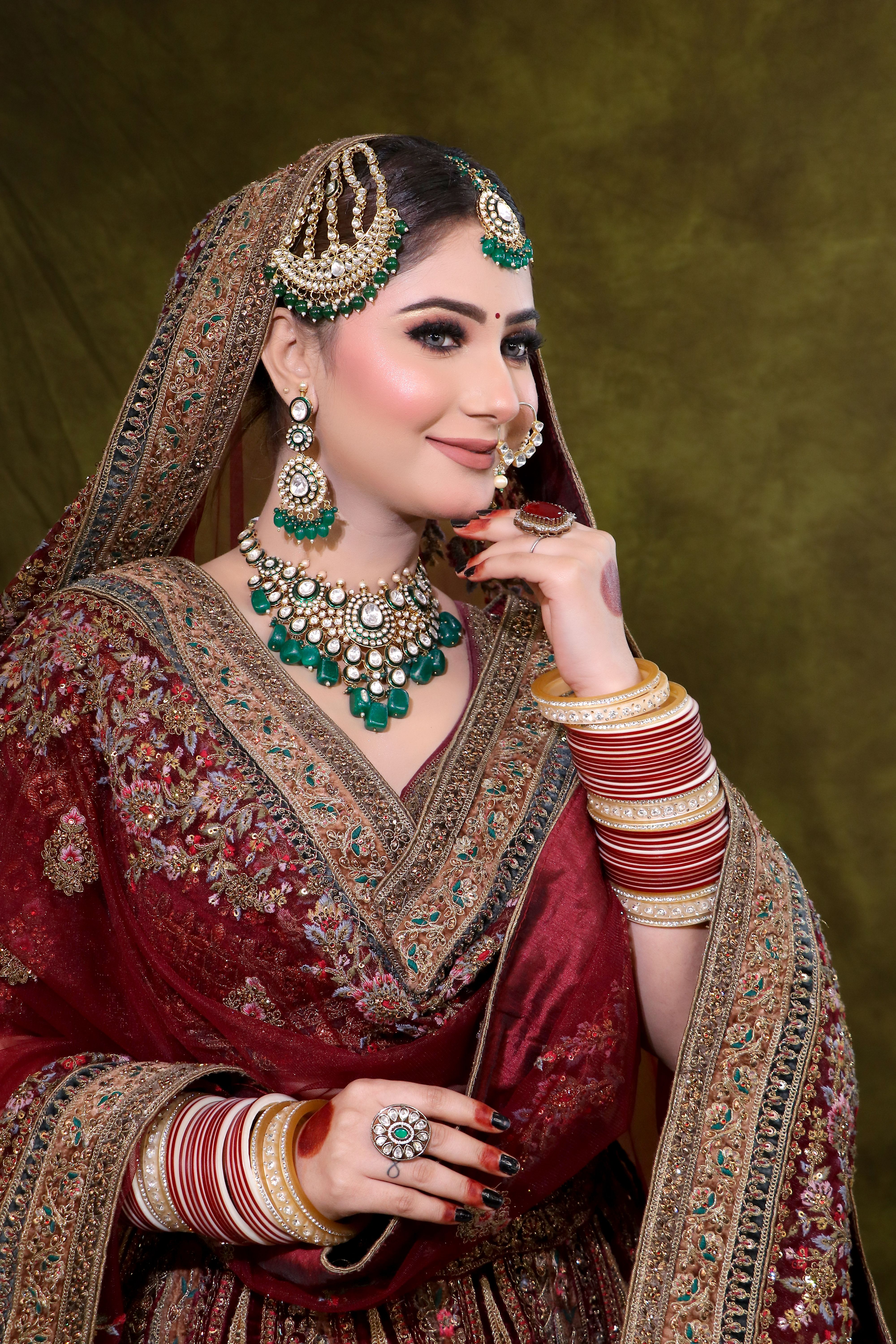 Beautiful bride in intricate maroon lehenga with stunning jewelry, posing gracefully.