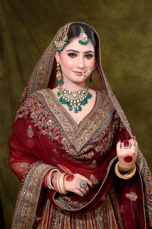 Free Elegant Indian bride in ornate red bridal gown and jewelry, smiling gracefully. Stock Photo