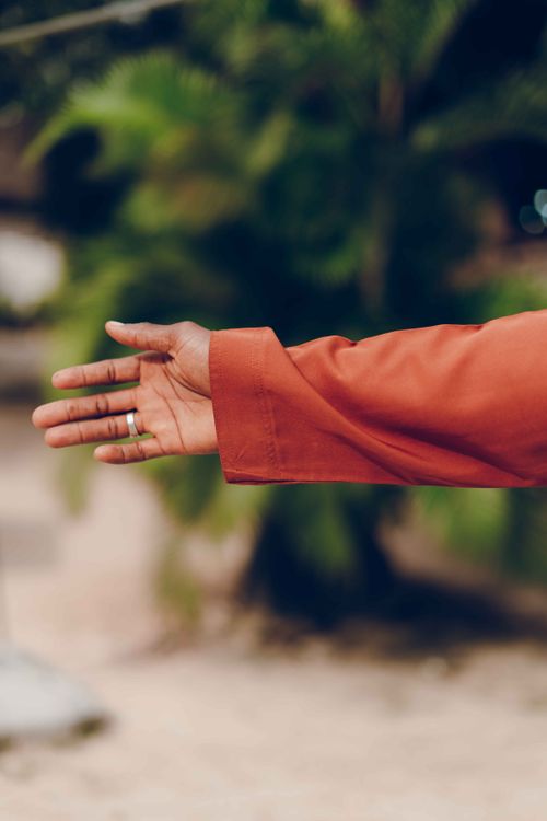 Free Close-up shot capturing the side view of a man's arm in a red sleeve outdoors, with a tropical background. Stock Photo