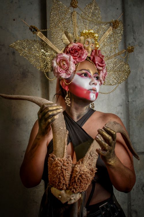 Free Artistic portrait of a costumed figure with a floral headdress and striking face paint, holding antlers. Stock Photo