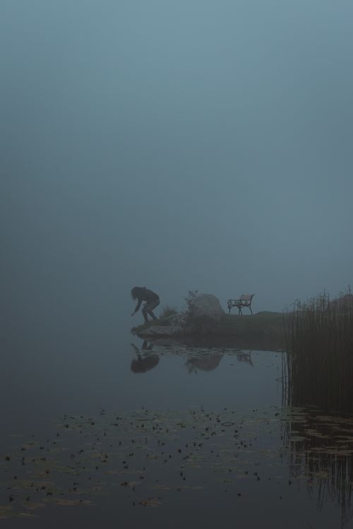 Free Shadowy figure jumping by a foggy lake with a bench and reeds, Styria, Austria. Stock Photo