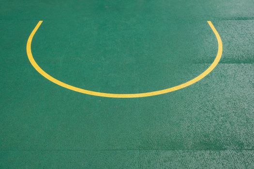A close-up view of a minimalist yellow marking on a green basketball court, showcasing geometric design.
