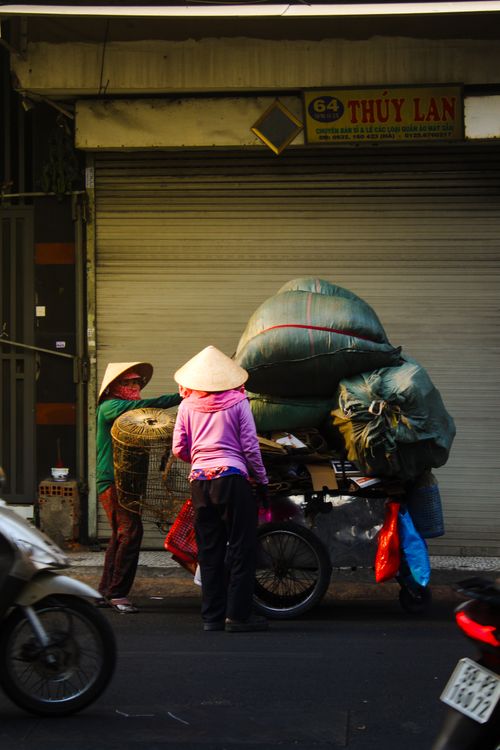 Free Traditional street vendors in Ho Chi Minh City balance goods on motorbikes in a bustling street corner. Stock Photo