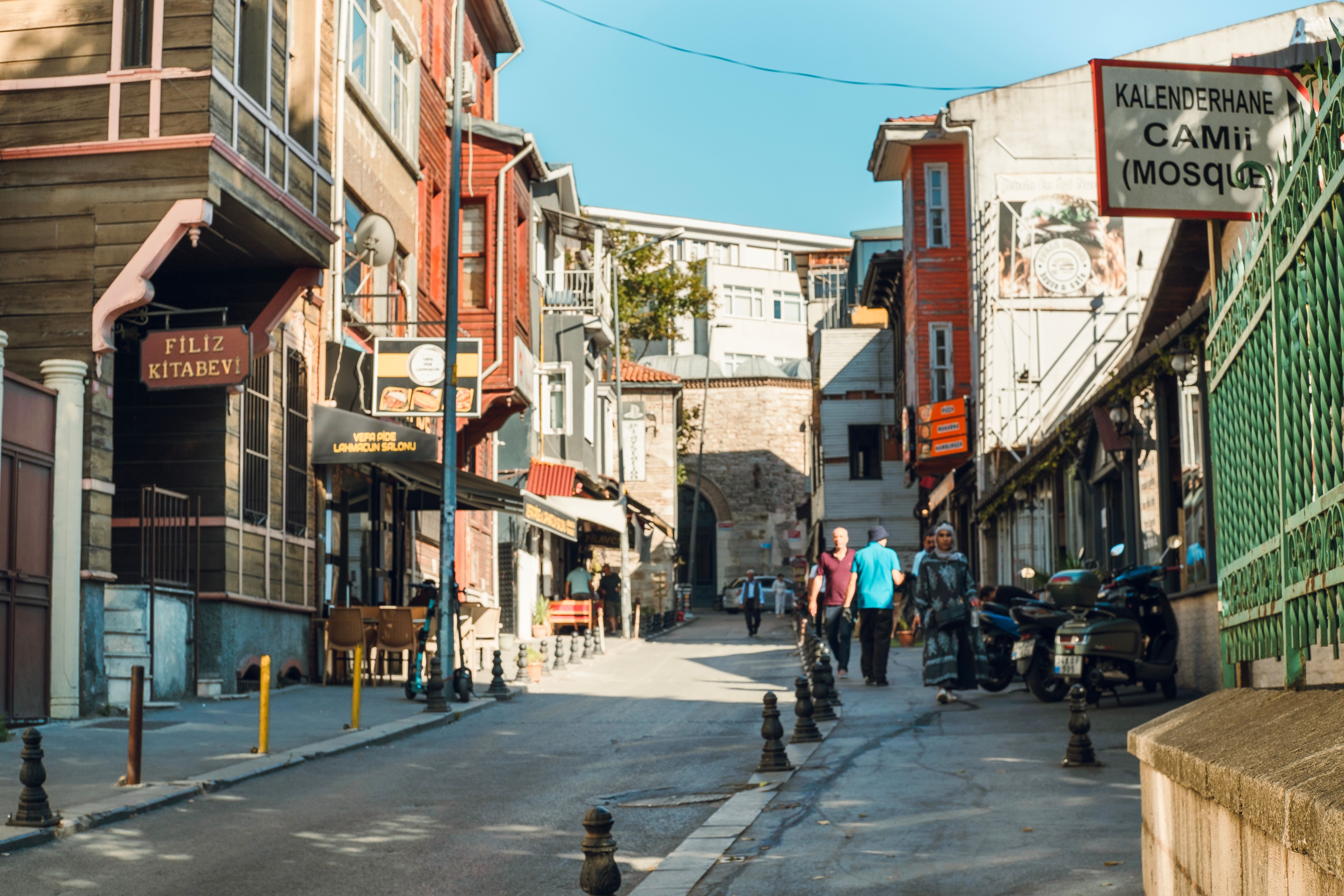 Quaint İstanbul street scene with traditional architecture, shops, and mosque sign, capturing local life.