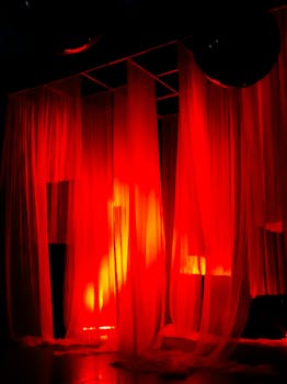 Vivid red curtains illuminated by stage lights create a dramatic atmosphere.