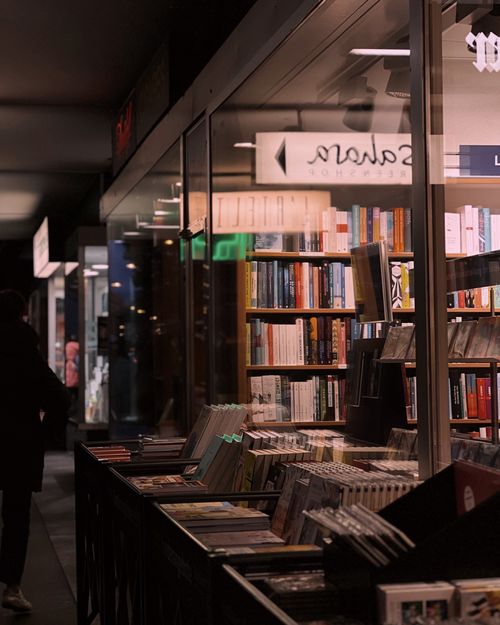 Free A warm-lit bookshop at night offers a cozy atmosphere with an array of books on display in the window. Stock Photo