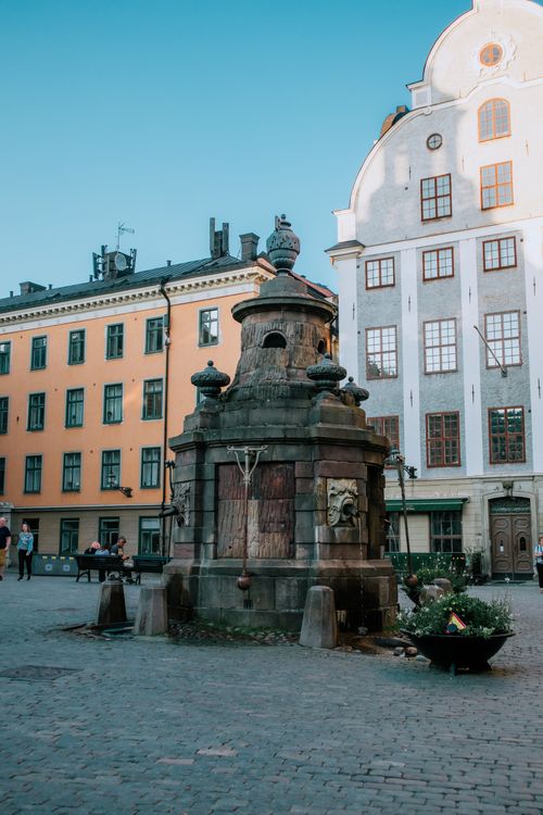 Free Charming medieval fountain in a historic European town square with surrounding architecture. Stock Photo