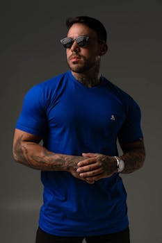 Strong man wearing sunglasses and a blue t-shirt, showcasing tattoos, confidence, and style.
