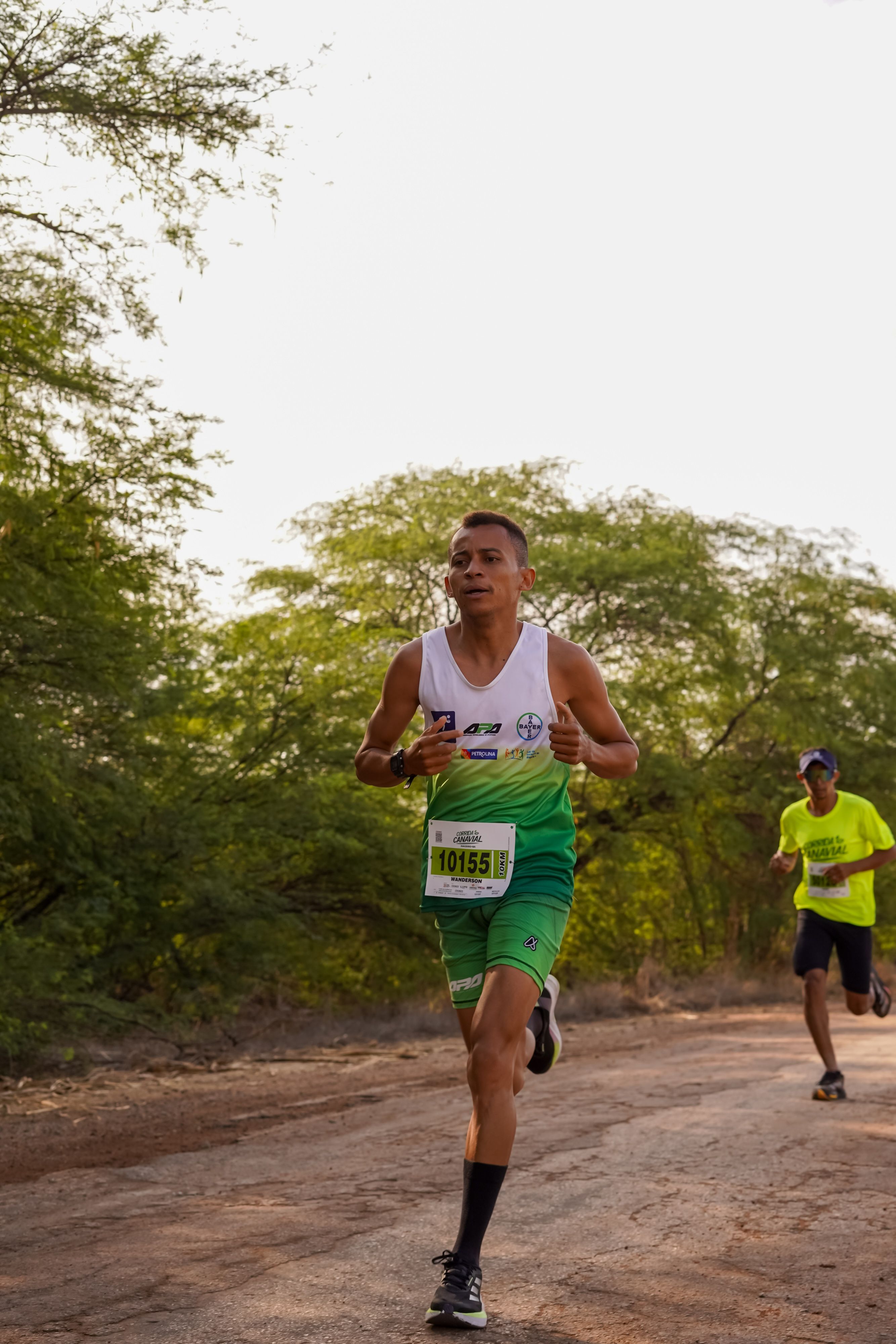 Two athletes running an outdoor marathon on a natural trail surrounded by greenery.