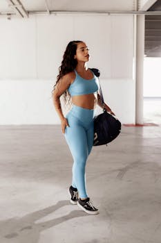 A woman in blue sportswear stands indoors holding a gym bag. Fitness lifestyle.