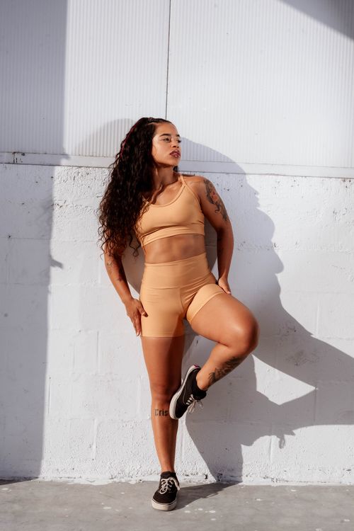 Free Confident athletic woman in a gym outfit posing against a sunlit wall, showing strength and style. Stock Photo