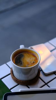 A steaming coffee cup on a cafe table beside a tablet and phone.