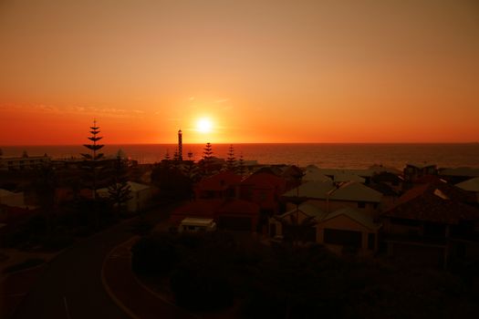 A stunning sunset over a coastal town with a lighthouse silhouette.
