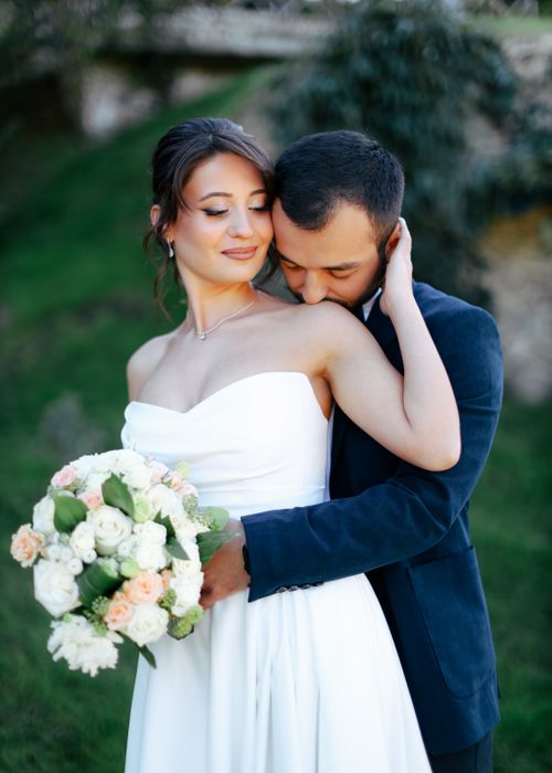 Free A romantic outdoor portrait of a wedding couple embracing, bride holding a floral bouquet. Stock Photo